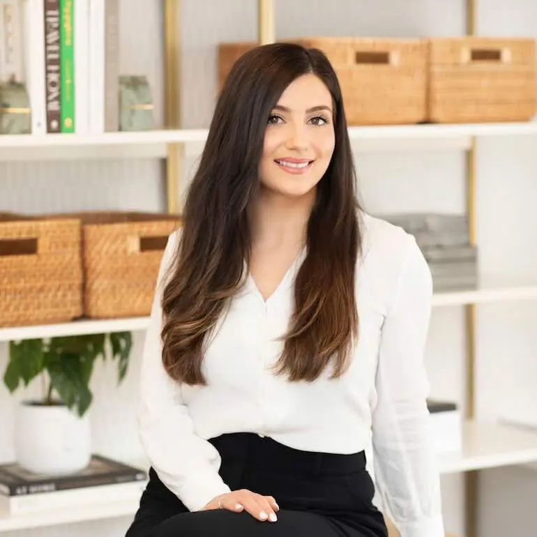 A woman in business clothes sitting on a desk.